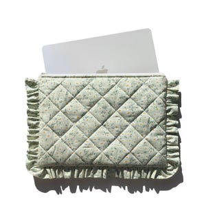 Könnte beinhalten: Eine hellgrüne, gesteppte Laptoptasche mit einem Blumenmuster aus kleinen gelben und weißen Blüten. Die Tasche hat einen gerüschten Rand und ein Laptop ist teilweise eingesetzt.
