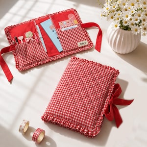 Op de afbeelding: Een rood-wit geblokte stoffen organizer met ruches aan de randen en een rood lint. De binnenzijde heeft vakjes met schrijfwaren, een kleine lolly en een label met de tekst Zehre. Een bijpassende gesloten organizer ligt ernaast.