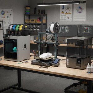 Peut inclure: Une scène d'atelier avec trois imprimantes 3D sur une table en bois. L'une est grise avec un support de filament noir, une autre est gris foncé avec un modèle de voiture blanche, et la troisième est une imprimante à résine transparente. Divers filaments colorés sont visibles.