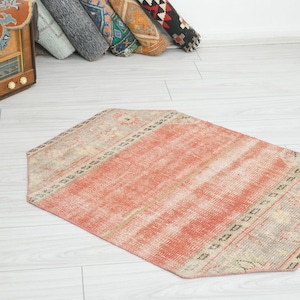 Peut inclure: Tapis octogonal vieilli, aux tons rouge et beige délavés. Le tapis présente un champ central rouge et une bordure à motifs. Il est posé sur un plancher en bois clair.