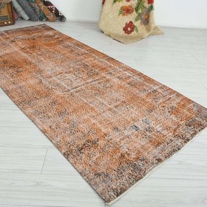May include: A rectangular area rug featuring a distressed, faded pattern in shades of burnt orange, charcoal gray, and cream. The design displays a worn, vintage-inspired texture with intricate, weathered motifs spread across the entire surface.