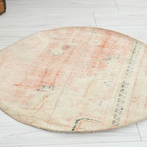 May include: A round area rug featuring a faded, distressed pattern in shades of cream, beige, and soft orange. The textile surface displays intricate, worn geometric and floral motifs with thin black linear accents throughout the circular design.