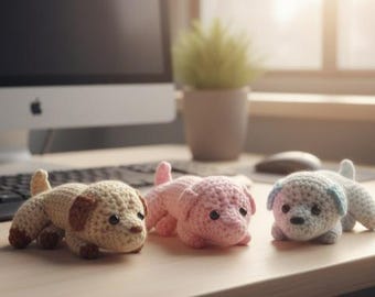 May include: Three handmade crochet dog toys in beige, pink, and blue. The beige dog has brown accents, the pink dog has a pink tail, and the blue dog has blue ears. The toys are lying on a wooden surface.