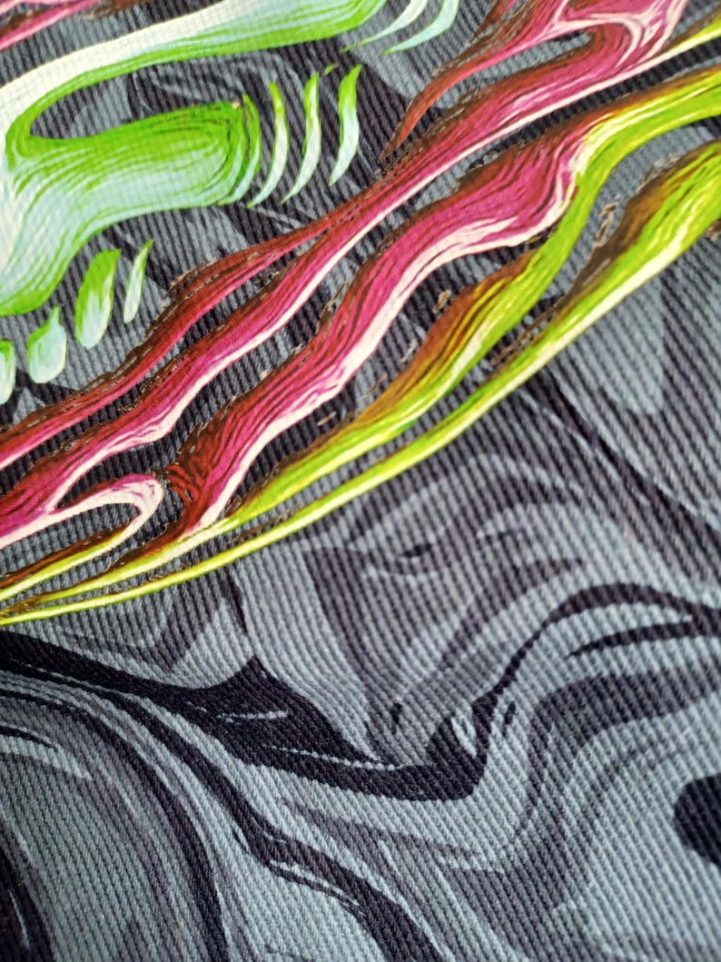 May include: Close-up of a textile with a swirling, abstract design. The pattern features flowing lines in shades of green, pink, and yellow against a textured gray background. The fabric appears to be denim or a similar material.