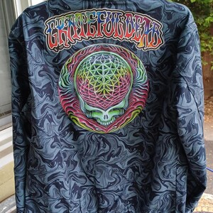 May include: A dark blue jacket with a swirling pattern. The back features a colorful skull design with a geometric pattern and the text "Grateful Dead" in rainbow colors. The jacket has a zipper and a collar.