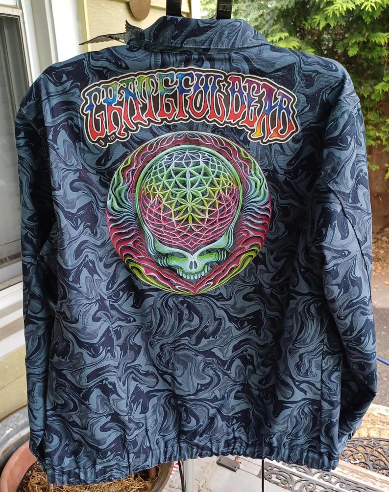 May include: A dark blue jacket with a swirling pattern. The back features a colorful skull design with a geometric pattern and the text "Grateful Dead" in rainbow colors. The jacket has a zipper and a collar.