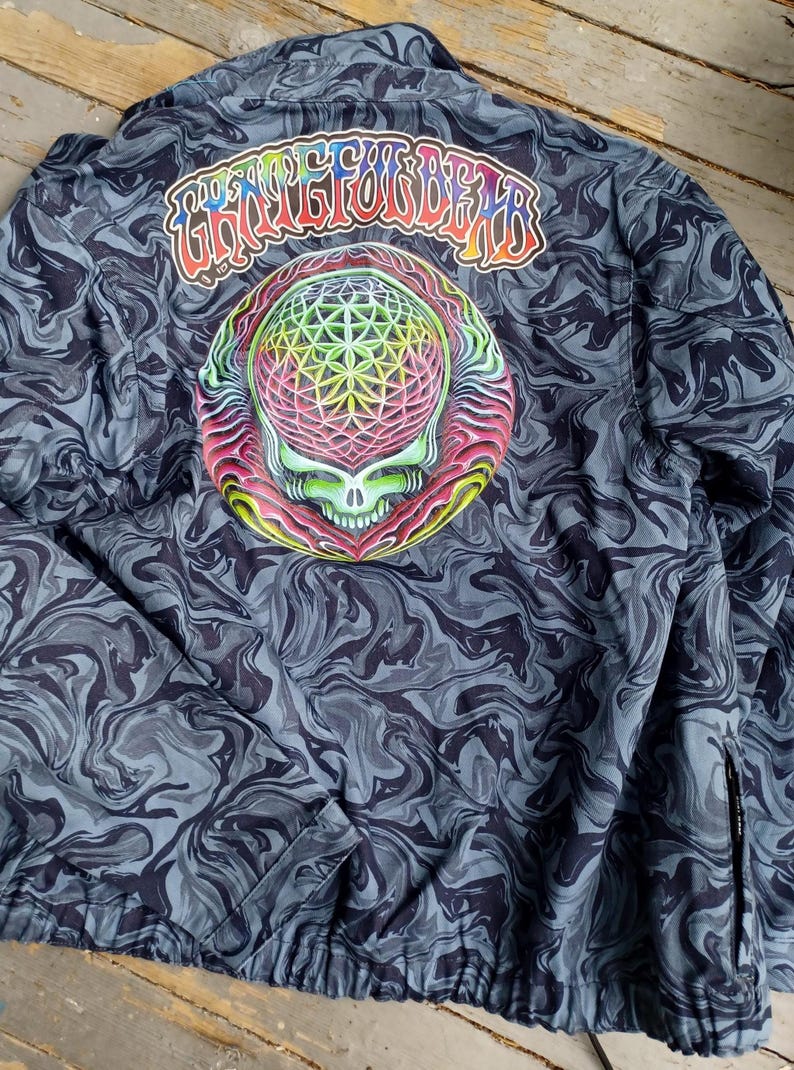 May include: A dark blue jacket with a swirling pattern and a colorful skull graphic on the back. The text "Grateful Dead" is arched above the skull. The jacket has a zipper and a drawstring at the bottom.