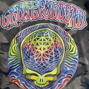 May include: A graphic design featuring a colorful skull with a geometric pattern and the text "Grateful Dead" in a rainbow arc. The design is set against a camouflage background.