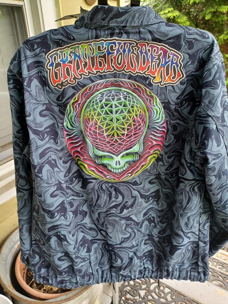May include: A dark blue jacket with a swirling pattern. The back features a colorful graphic of a skull and geometric design, with the text "Grateful Dead" above it. The jacket has a drawstring at the bottom.