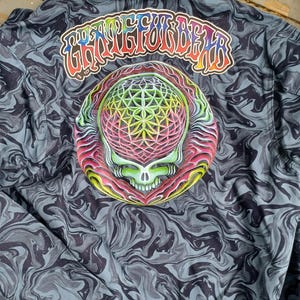 May include: A button-up jacket with a swirling gray and black pattern. The back features a colorful graphic of a skull with a geometric design and the text "Grateful Dead" in rainbow colors.