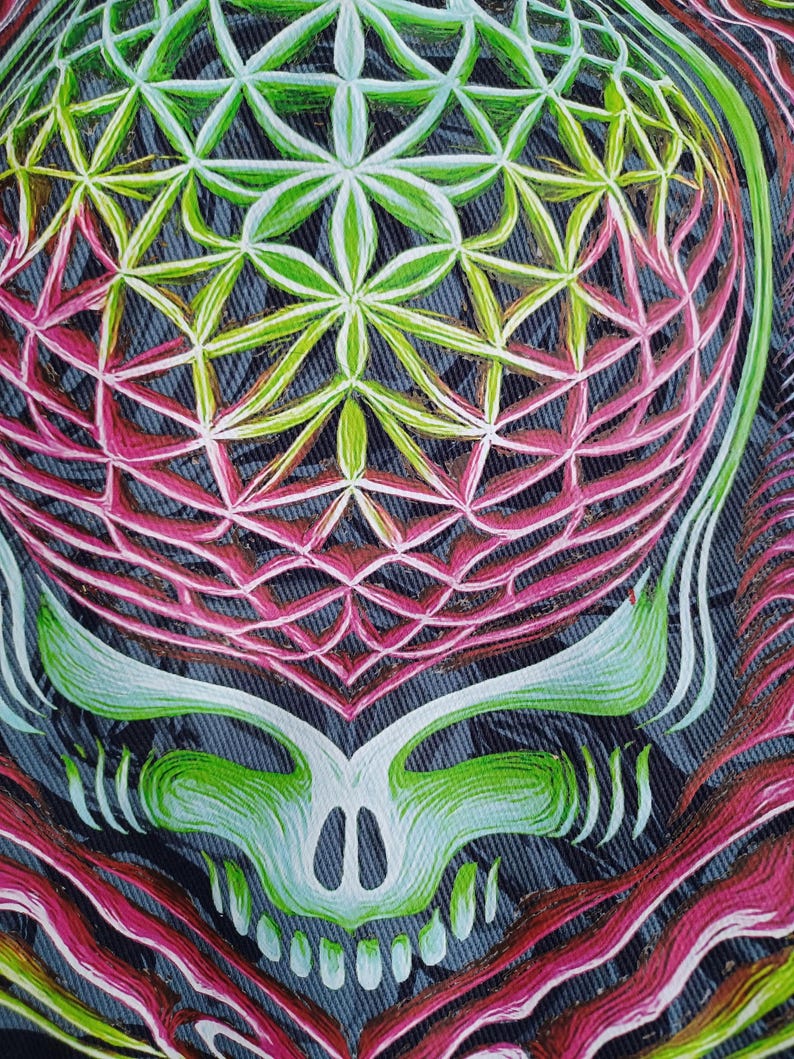 May include: Close-up of a colorful, stylized skull design. The artwork features a geometric pattern in shades of green, pink, and white, set against a denim-like background. The skull's features are outlined in white and green.