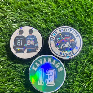 May include: Three circular hockey pucks with holographic accents. One features two players in jerseys numbered 81 and 24. Another displays a hawk logo with the text Briar University Hawks. The third is green with the name Kavanagh and number 13.