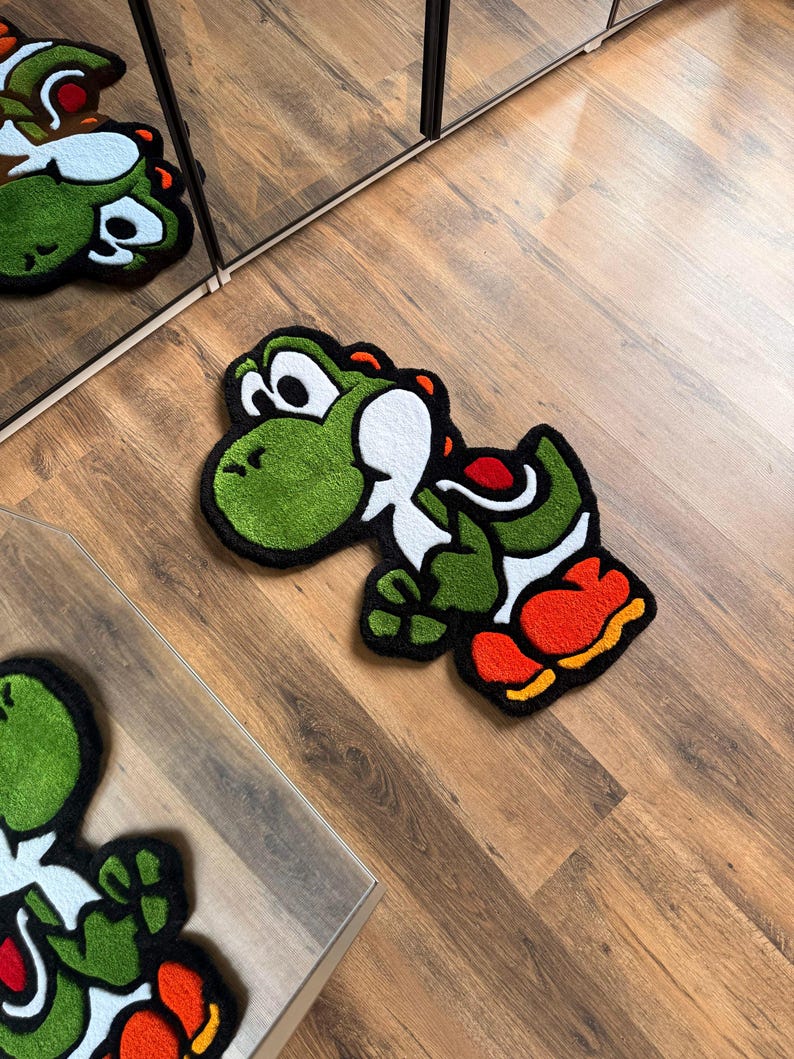 May include: A green, white, red, and orange Yoshi rug. The rug is in the shape of the character Yoshi from the Super Mario video game series. The rug is on a wooden floor.