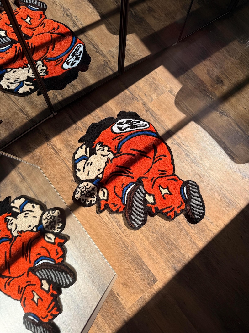 May include: A red and orange rug featuring a cartoon character in a kneeling position. The rug has black, white, and blue accents, and is placed on a wooden floor. The image is taken from an elevated angle, with a mirror reflecting the rug.