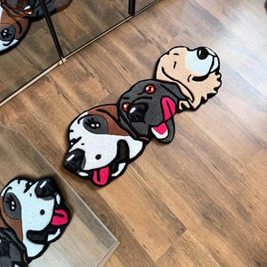 May include: A collection of dog-shaped rugs in various colors and patterns. The rugs feature detailed designs of dog faces with open mouths and tongues. The rugs are placed on a wooden floor.
