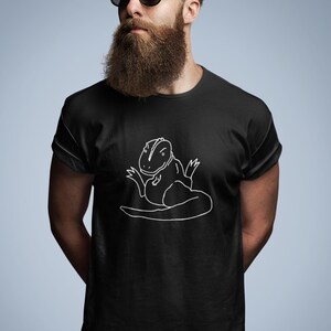 May include: Black t-shirt with a white outline drawing of a lizard-like creature. The design is centered on the shirt. The t-shirt has short sleeves and a crew neck. The background is a solid light blue.