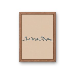 Może przedstawiać: Oprawiony wydruk z minimalistyczną ilustracją linii horyzontu w ciemnoniebieskim kolorze na beżowym tle. Grafika przedstawia architektoniczne sylwetki budynków i piramid. Rama wykonana jest z jasnobrązowego drewna.