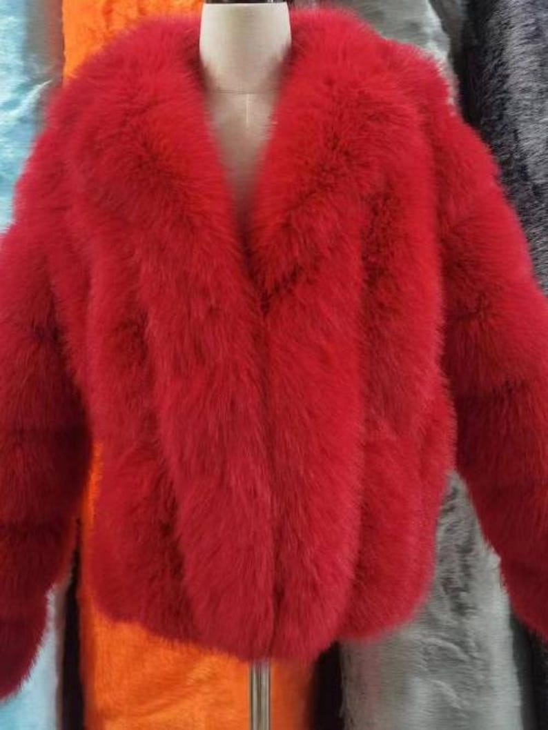 May include: A vibrant red faux fur jacket with a wide collar and long sleeves. The jacket is displayed on a mannequin, showcasing its plush texture and bold color. The jacket's design features a V-neckline and a cropped length.