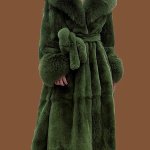 May include: An olive green faux fur coat with a large collar, cuffs, and a matching belt. The coat has a plush texture and a flowing silhouette. This long coat is designed to be worn as outerwear, offering a luxurious look.
