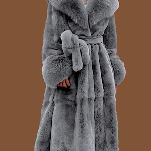 May include: A long, grey faux fur coat with a large collar and matching belt. The coat features long sleeves with fur cuffs. The coat is designed to be worn as outerwear and provides warmth and style.