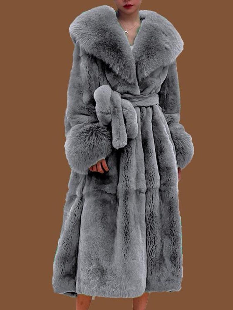 May include: A long, grey faux fur coat with a large collar and matching belt. The coat features long sleeves with fur cuffs. The coat is designed to be worn as outerwear and provides warmth and style.