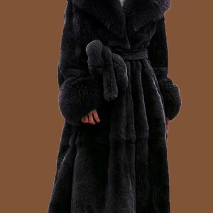 May include: A full-length black faux fur coat with a large collar and cuffs. The coat is belted at the waist with a matching tie. The coat has a luxurious appearance, suitable for formal wear. The coat is floor-length.