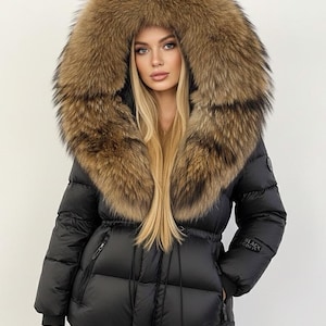 May include: Black puffer jacket featuring a large hood trimmed with brown fur. The jacket has a drawstring waist, zipped pockets, and the text "BLACK GRAPES" on the sleeve. A fashionable winter coat.