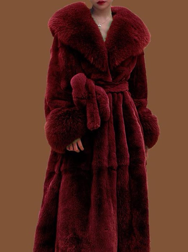 May include: A long, burgundy faux fur coat with a wide collar and matching cuffs. The coat features a tie belt at the waist and a full, flowing skirt. The plush texture and rich colour create a luxurious look.