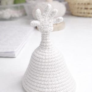 May include: A handmade, white crochet sculpture of a hand atop a conical base. The sculpture is made with a tight stitch, and the hand has five fingers. The piece is set against a soft, neutral background.