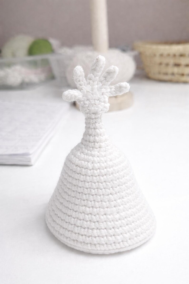 May include: A handmade, white crochet sculpture of a hand atop a conical base. The sculpture is made with a tight stitch, and the hand has five fingers. The piece is set against a soft, neutral background.