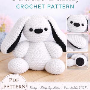 May include: A white crochet bunny with black accents, including the inner ears and nose. The bunny is sitting on a wooden surface. The image also includes a PDF pattern with the text "The Cuddle Bunny CROCHET PATTERN".