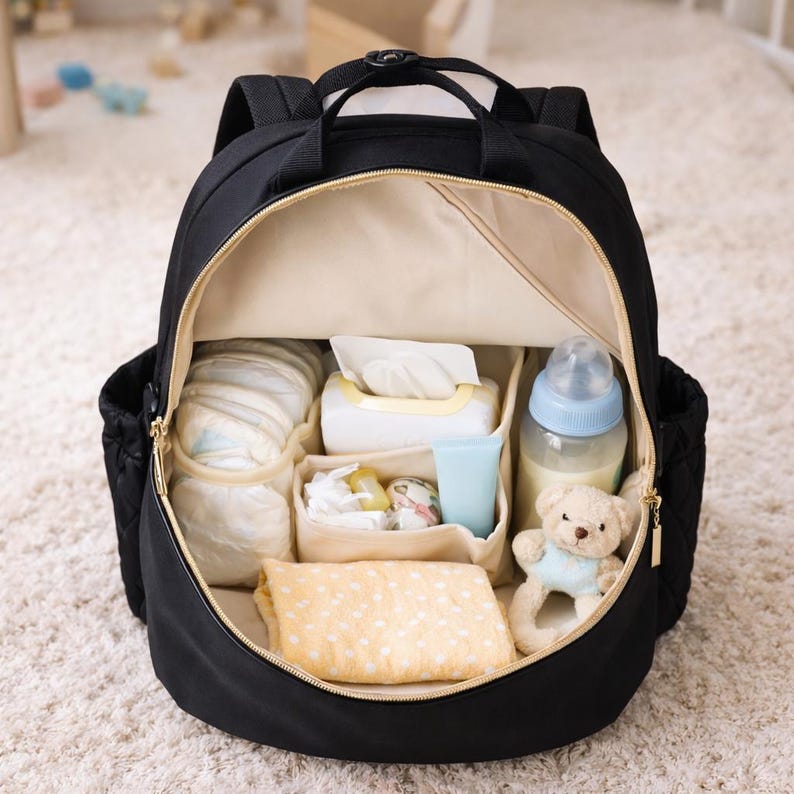 Open black diaper backpack with baby essentials inside including bottles, diapers and wipes