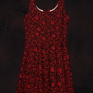 May include: A red and black floral patterned sleeveless dress. The dress features a scoop neckline with a white trim. The text "Realm of Mythology" is at the bottom. The dress has a fit and flare design, suitable for various occasions.