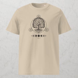 May include: Beige t-shirt featuring a black graphic of a tree within a circle, geometric shapes, and phases of the moon. The design is centered on the front of the shirt. The shirt has short sleeves and a crew neck.