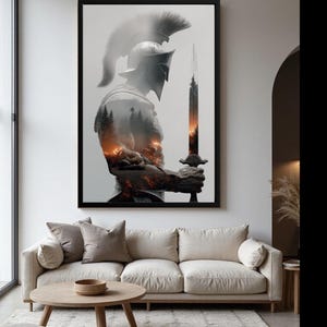 Puede incluir: Una obra de arte enmarcada que representa a un guerrero espartano sosteniendo una espada. El guerrero está representado en escala de grises, con un bosque y un paisaje de fuego sutilmente integrados. La obra está sobre un sofá beige.