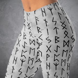 May include: White leggings with a repeating pattern of black runic symbols. The leggings are form-fitting and appear to be made of a stretchy material. The background is a solid gray color.