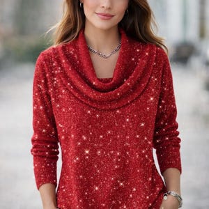 Può includere: Un maglione rosso con collo a imbuto e maniche lunghe. Il maglione ha un effetto scintillante e glitterato. La persona indossa una collana e un braccialetto d'argento. La persona indossa pantaloni bianchi.