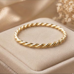 May include: A thin, circular ring crafted from polished yellow gold. The band features a continuous twisted rope design, creating a textured, spiraling appearance that catches the light along its entire circumference.