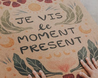 May include: A yoga mat with a cork-like texture, featuring floral and leaf illustrations in burgundy, green, and yellow. The mat has the French phrase "JE VIS le MOMENT PRESENT" in black lettering. The mat is rectangular.