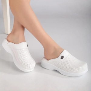 Può includere: Zoccoli bianchi traforati con punta arrotondata e suola spessa. Gli zoccoli hanno un design slip-on e un piccolo emblema decorativo sulla parte superiore. Le scarpe sono realizzate in materiale leggero.
