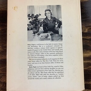 May include: Vintage book cover featuring a black and white photo of Betty Pepis, an interior design expert. The cover includes text about her career as a columnist, editor, and consultant. The background is a dark wood surface.