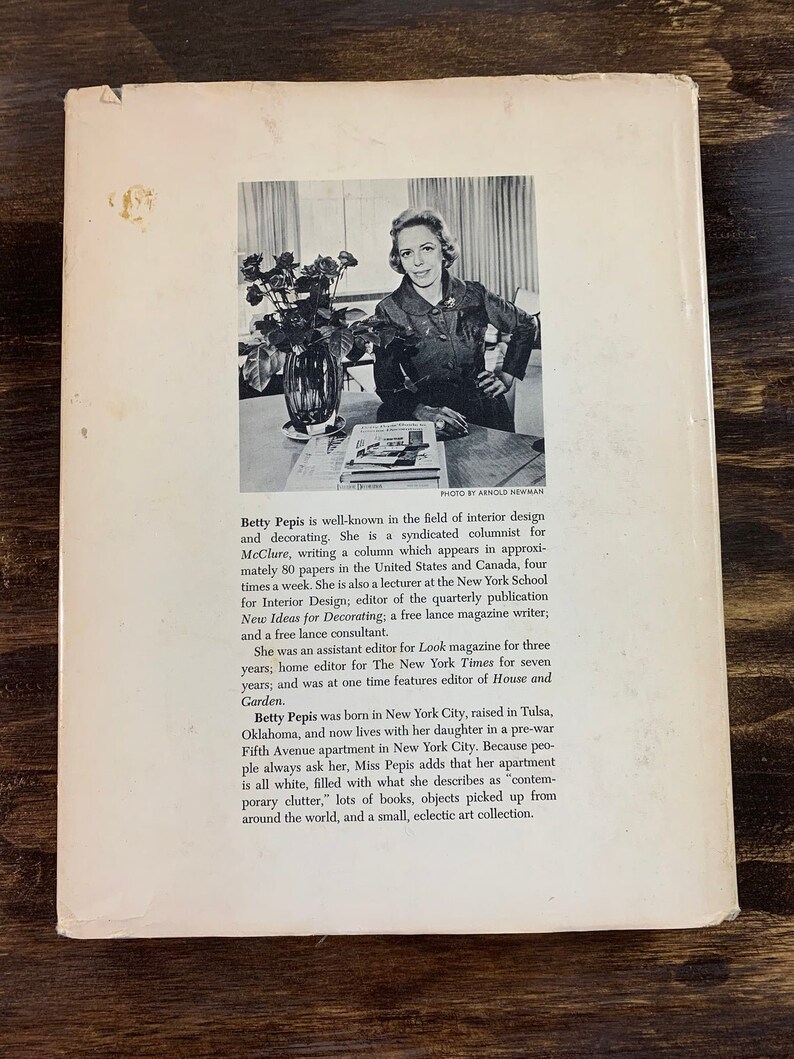 May include: Vintage book cover featuring a black and white photo of Betty Pepis, an interior design expert. The cover includes text about her career as a columnist, editor, and consultant. The background is a dark wood surface.