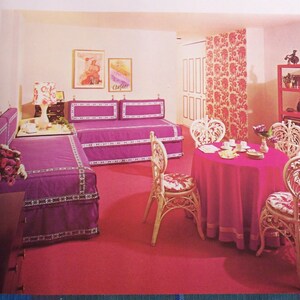 May include: A retro-style interior with a vibrant color scheme. The room features a magenta carpet, matching furniture, and a round dining table. Decorative chairs surround the table, and artwork adorns the walls. A patterned curtain and a pink shelving unit complete the scene.