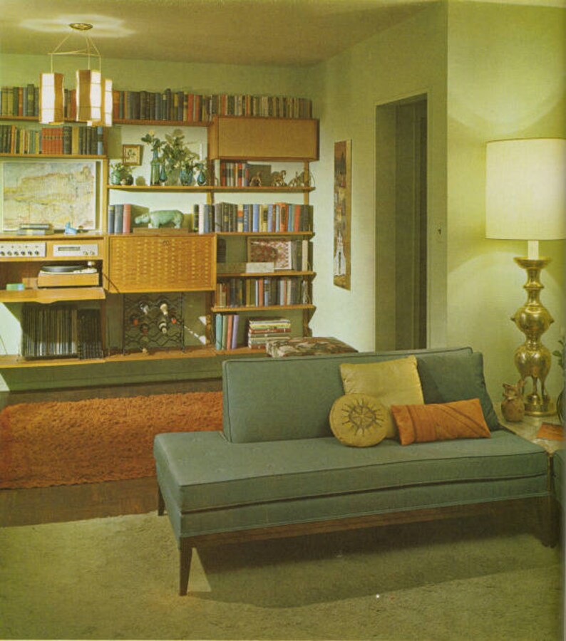 May include: A mid-century modern living room with a teal sofa, wooden bookshelves filled with books, and a shag rug. A gold lamp and decorative pillows add color to the space. The room has a retro aesthetic.