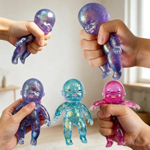 May include: Five glittery baby dolls in various colors: purple, blue, and pink. The dolls are held in hands, showcasing their translucent bodies and sparkling details. The dolls have closed eyes and open mouths.