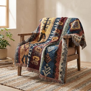 Op de afbeelding: Een kleurrijke geweven deken over een houten fauteuil. De deken heeft een geometrisch patroon in blauw, geel, rood en bruin, met gefranjerde randen. De stoel staat op een gestreept tapijt.