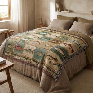 May include: A woven throw blanket featuring a repeating pattern of various fish illustrations in a grid. The blanket has a fringed edge and is primarily beige, green, and brown. The blanket is draped over a bed with neutral-toned bedding.