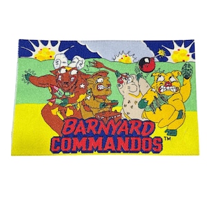 May include: A rectangular patch featuring the text "BARNYARD COMMANDOS" with cartoon animal characters. The characters are in shades of red, brown, yellow, and white, set against a green and yellow background with a blue sky.