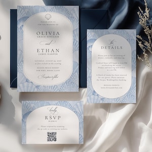 May include: A wedding stationery set featuring a main invitation, a details card, and an RSVP card with a QR code. Each piece has a light blue seashell pattern border and a central arched white panel with black serif text on a dark blue envelope.