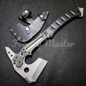 May include: A tactical axe with a black handle and a silver blade, accompanied by a black leather sheath. The axe features a unique design with a pointed end and a circular cutout. The text "Forging Master" is visible.